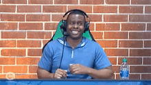 a man wearing headphones is sitting at a table with a bottle of water in front of a brick wall .