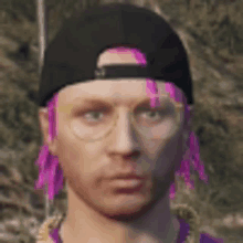 a man with pink dreadlocks and glasses is wearing a black hat and a purple shirt .