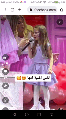 a little girl is singing into a microphone while her mother looks on