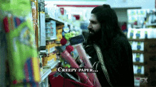 a man with long hair and a beard is standing in a store and holding a basket of creepy paper