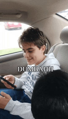 a boy sitting in the back seat of a car playing a video game with the words dumbahh above him