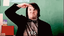 a man in a suit and bow tie is making a funny face in front of a green board .