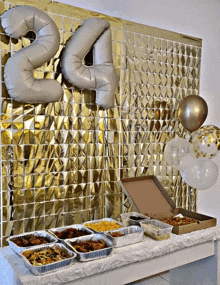 a table full of food and balloons with the number 24 on the wall behind it