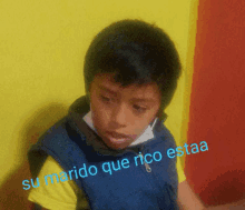 a young boy wearing a blue vest with the words su marido que rico estaa on the bottom