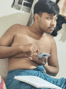 a shirtless man is sitting on a bed holding a cell phone