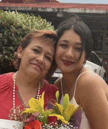 two women are posing for a picture with a bouquet of flowers between them