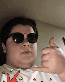 a boy wearing sunglasses and a peace sign shirt giving a thumbs up