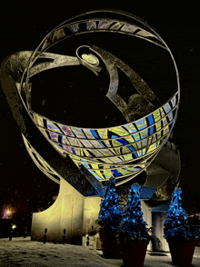 a stained glass sculpture is lit up at night with a few potted plants in front of it