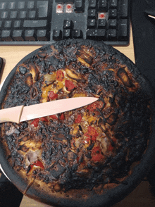 a burnt pizza sits on a desk with a knife in it