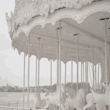 a white merry go round with horses on it is sitting next to a body of water .