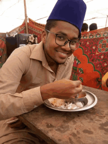 a man wearing glasses and a blue hat is eating a plate of food