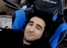 a man is laying in a blue and black gaming chair with headphones on .