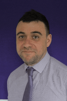 a man in a purple shirt and purple tie stands in front of a purple wall