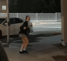 a man is standing on a sidewalk in front of a white car .