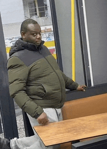 a man in a green jacket is standing in front of a table .