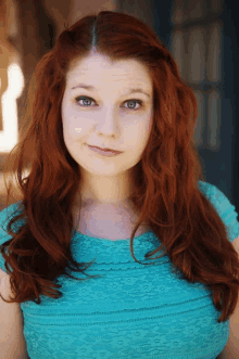 a woman with long red hair is wearing a blue top