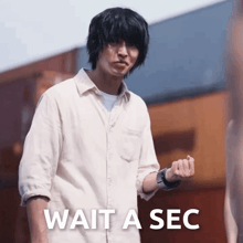 a man in a white shirt stands in front of a sign that says " wait a sec "