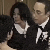 a man in a tuxedo and a woman in a black dress are talking to each other .