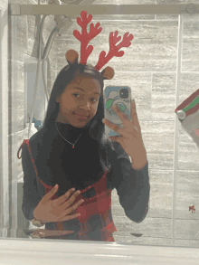 a girl wearing reindeer antlers takes a picture of herself in the mirror