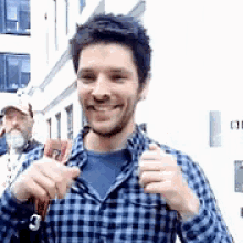 a man in a plaid shirt is smiling and holding a key while standing in front of a building .