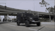 a black armored vehicle drives down a street under a bridge