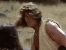 a man without a shirt is standing in a field with a backpack .