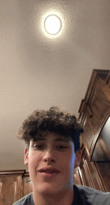 a young man with curly hair looks at the camera in front of a light on the ceiling