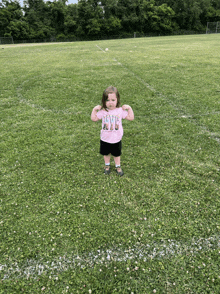 a little girl flexes her muscles in a field wearing a shirt that says i love nyc