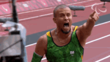 a man wearing a green and yellow tank top with a brazilian flag on it is celebrating on a track