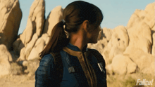 a woman in a ponytail is standing in front of rocks with the word fallout on the bottom