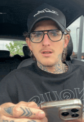 a man with glasses and a tattoo on his face holds a phone