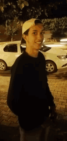 a young man wearing a white hat and a black shirt is smiling in front of a white car