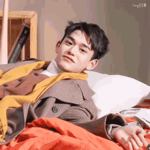 a young man in a trench coat is laying on a bed with a book on the shelf behind him