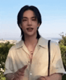 a young man with long hair is wearing a yellow shirt and standing in front of a blue sky .