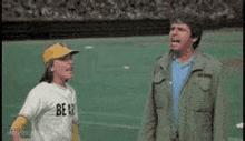 a man and a boy are standing on a baseball field . the boy is wearing a jersey that says be 13 .