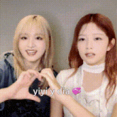 two girls are making a heart shape with their hands and the words yiyi y dia are written above them .