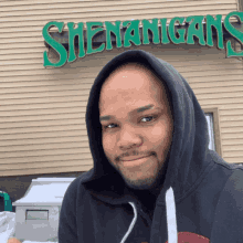 a man wearing a black hoodie is standing in front of a sign that says shenanigans