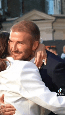 a man in a suit is hugging a woman in a white jacket with a diamond ring on her finger ..