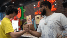 a man in a yellow shirt shakes hands with another man in a white shirt in front of a neon sign that says eat up at