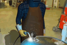 a man wearing a welding helmet and apron is welding a blue object