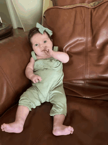 a baby is sitting on a leather couch with her hand in her mouth