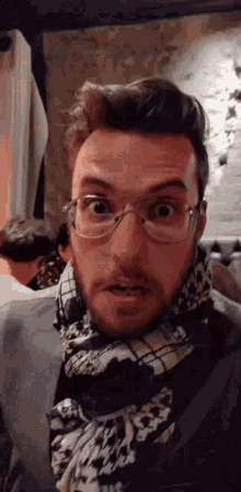 a man wearing glasses and a scarf is making a face .