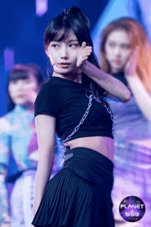 a girl in a black crop top and pleated skirt stands on a stage with planet 999 written on the bottom