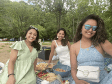 three women posing for a picture while sitting on a blanket