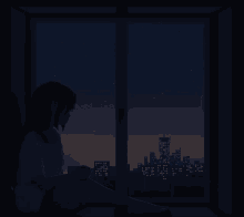 a woman is sitting in front of a window looking out at the city at night