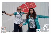 two women are posing for a photo in front of a sign that says " you 're olympic games "