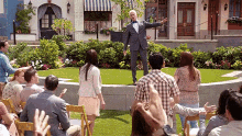 a man in a tuxedo and bow tie is standing on a stage in front of a crowd of people .