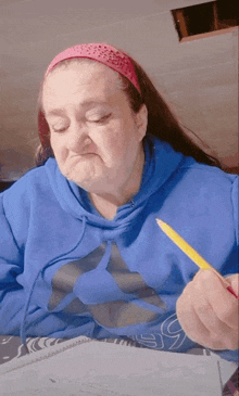 a woman in a blue hoodie is writing in a notebook while holding a pencil .