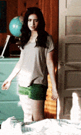 a woman in a grey shirt and green shorts stands in front of a globe