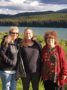 three women posing for a picture with a lake in the background